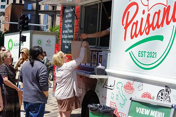 A woman takes a bag of food from the window of a food truck
